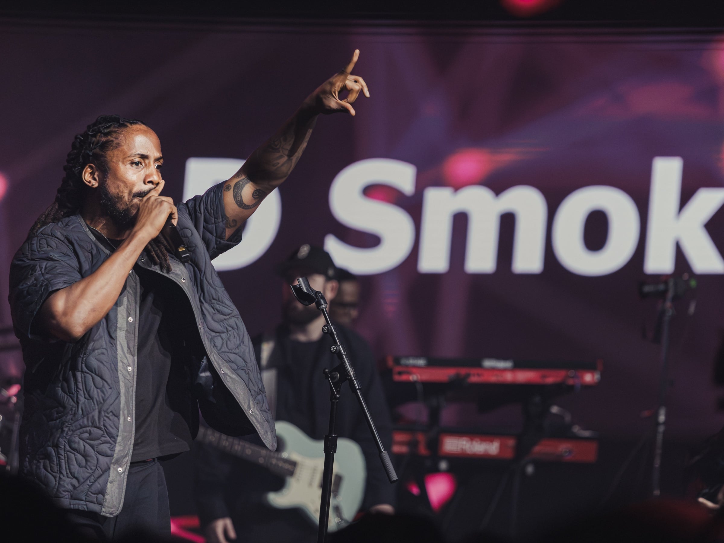 Performer holding a microphone and raising an arm against a purple stage backdrop
