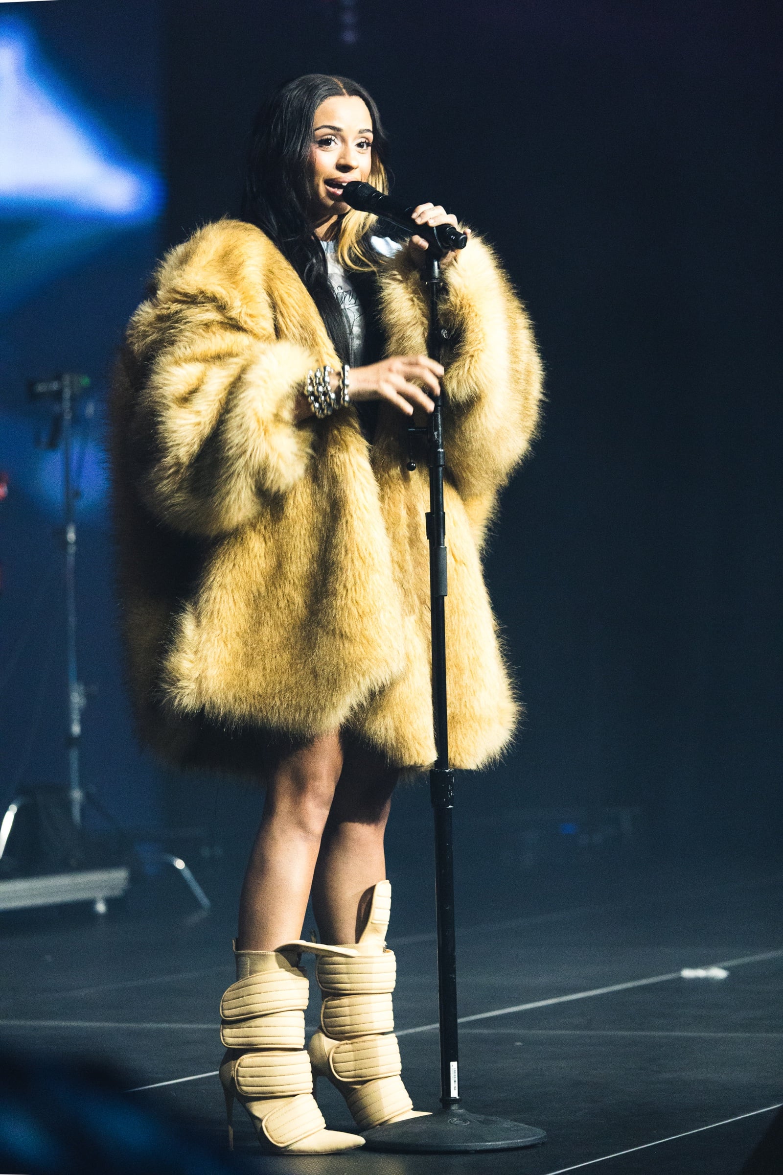 Singer in a yellow coat holding a microphone on a dark blue-lit stage