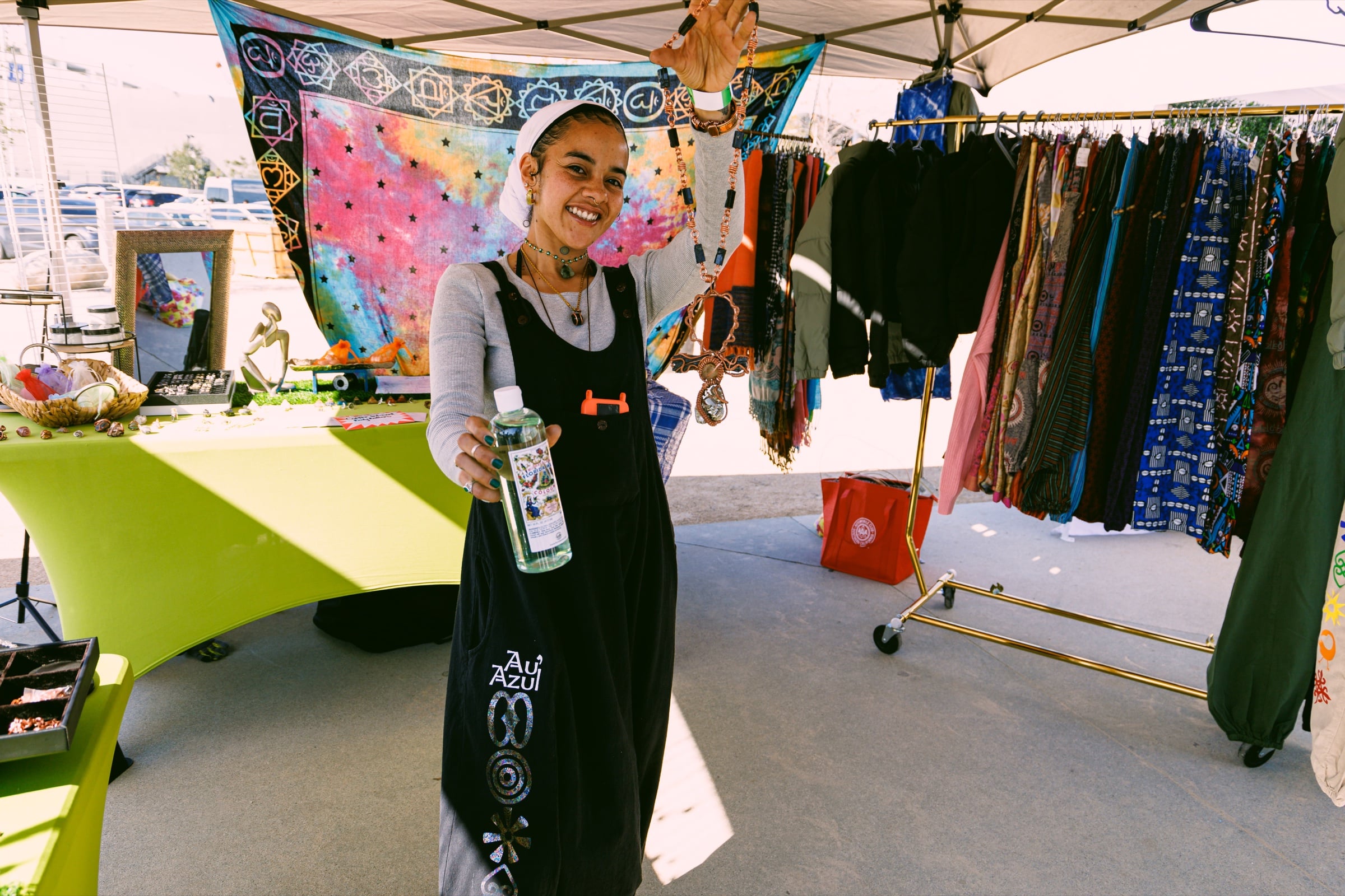 Vendor smiling and holding up an object beneath a canopy surrounded by merchandise