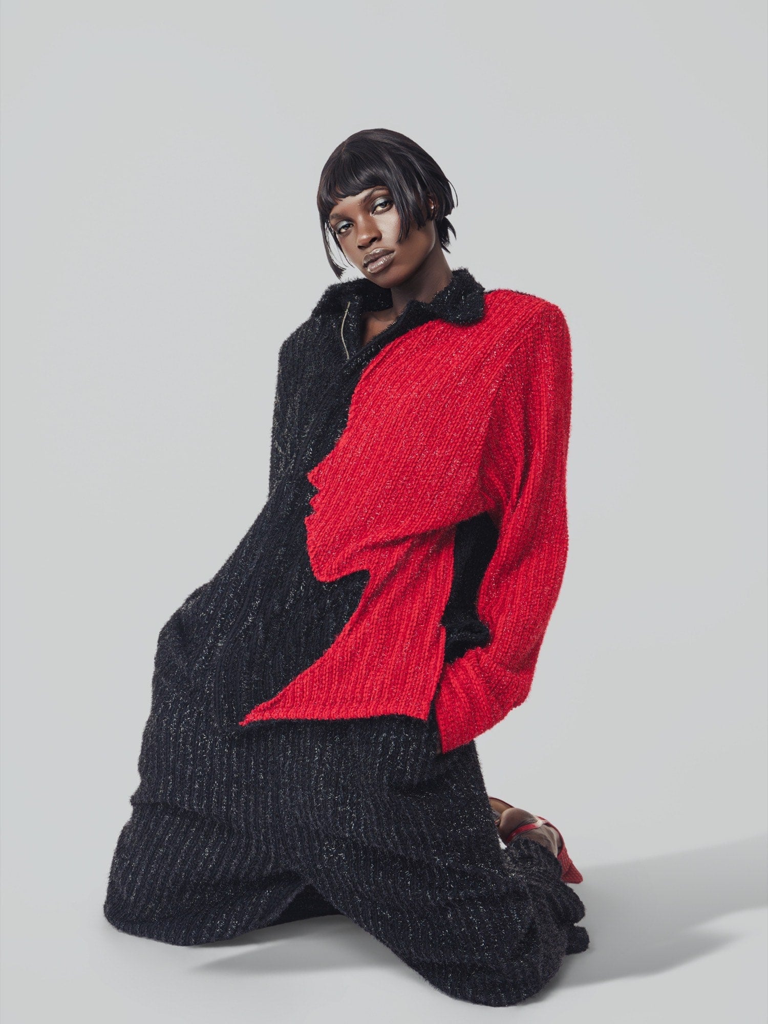 Kneeling model in a black and red jacket against a gray backdrop