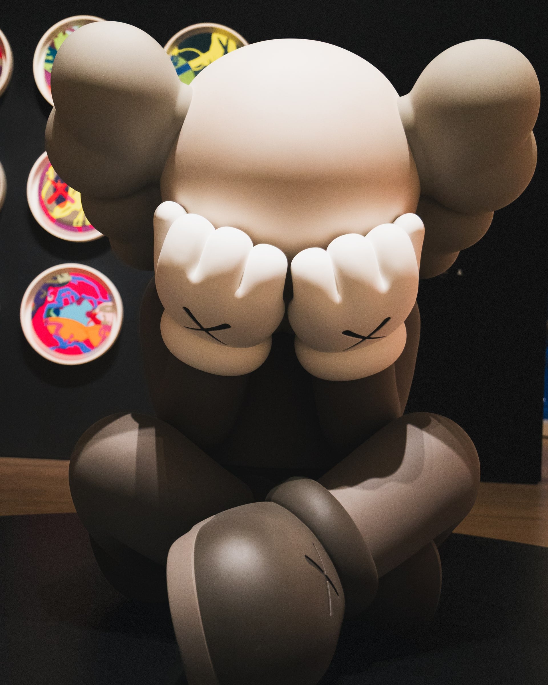 Large seated sculpture covering its eyes inside an art gallery