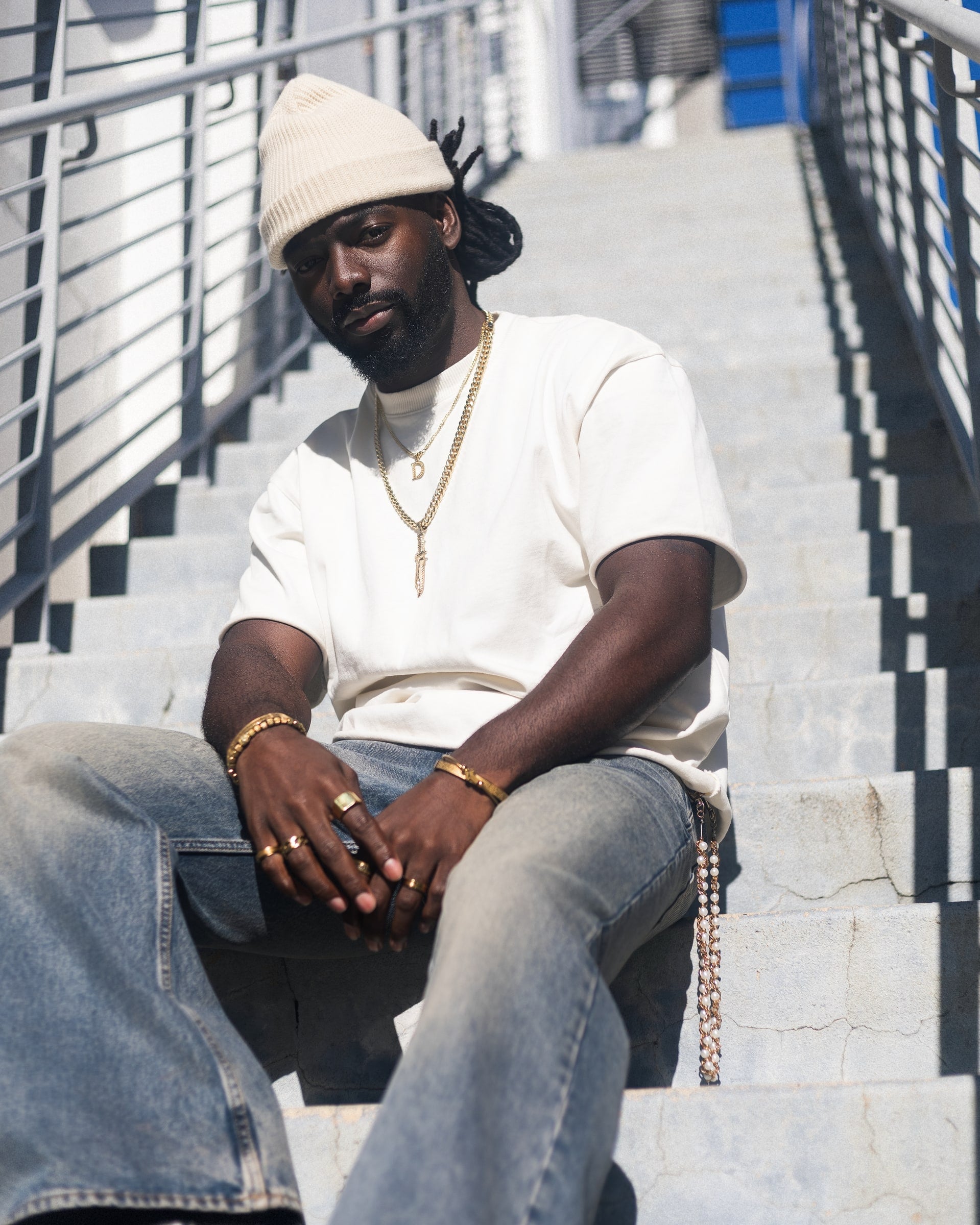Man in a white T-shirt and knit cap seated on outdoor stairs