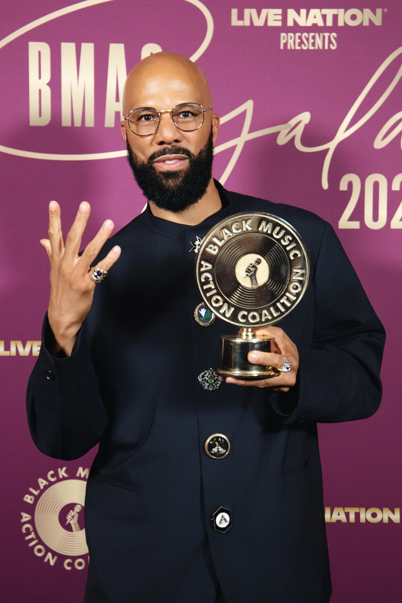Guest wearing glasses and a black jacket holding a Black Music Action Coalition award and raising a hand